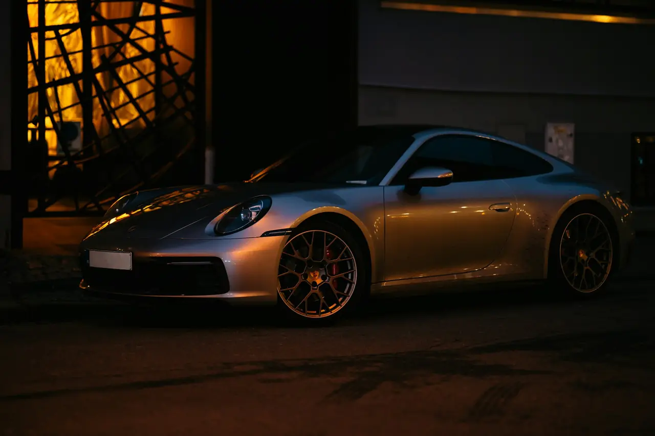 Porsche 911 argent garée de nuit, éclairée par une lumière chaude