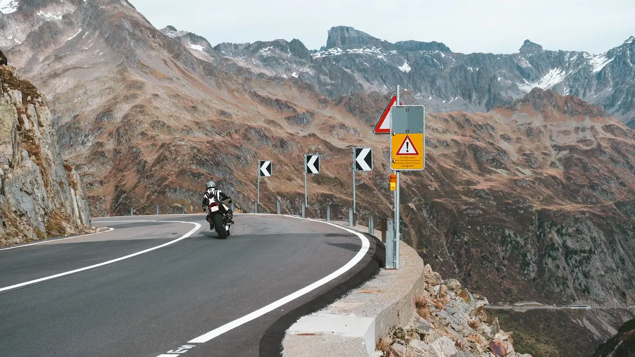Un motard dans un virage de col, balises et panneau de danger en bord de route