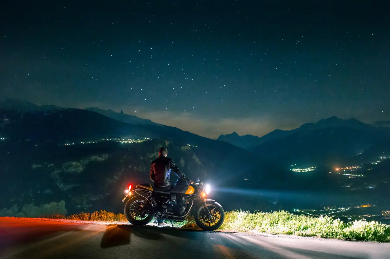 Un motard arrêté de nuit au-dessus d’une vallée éclairée