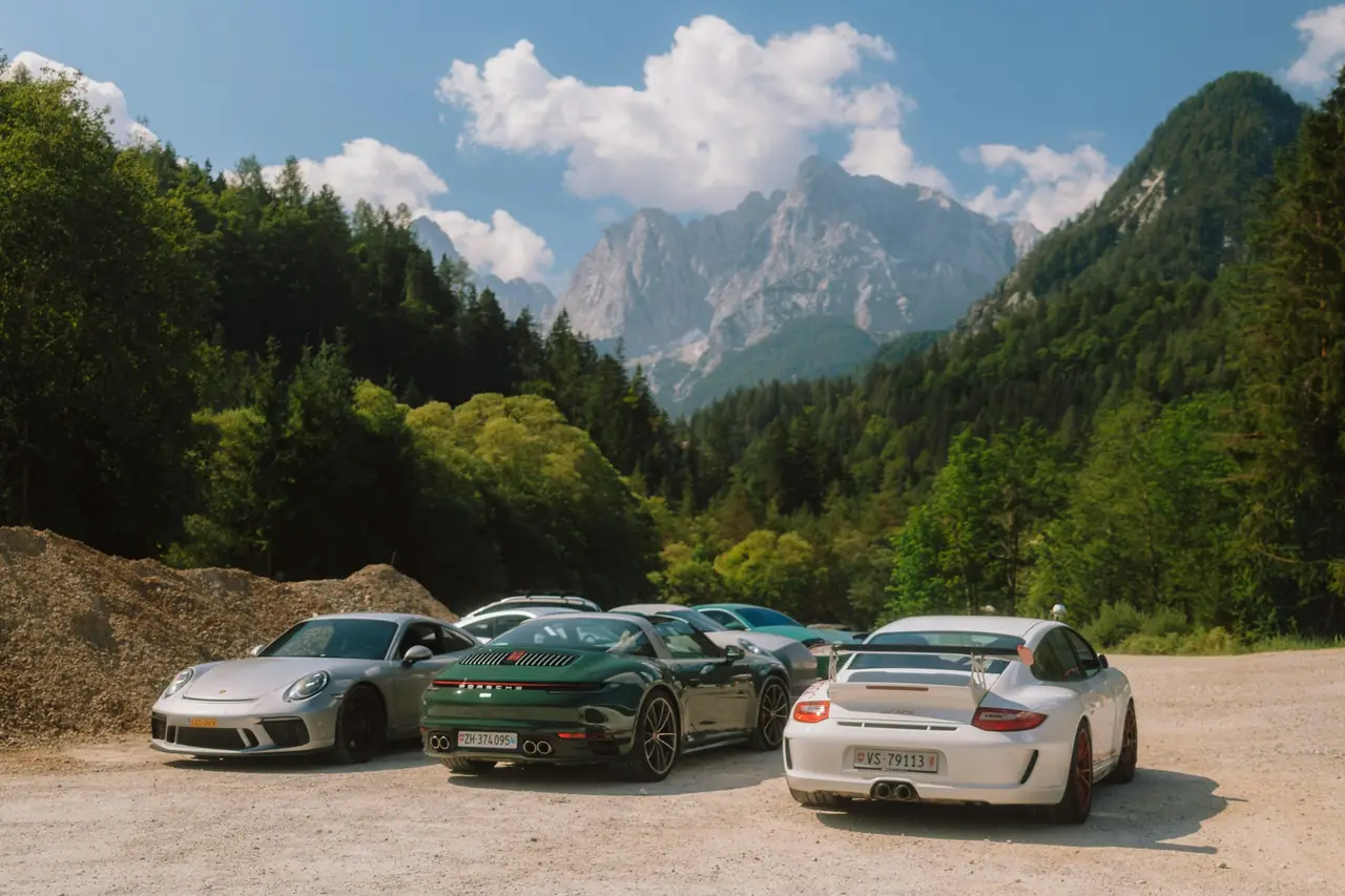 Trois Porsche garées sur un parking de gravier au pied de montagnes